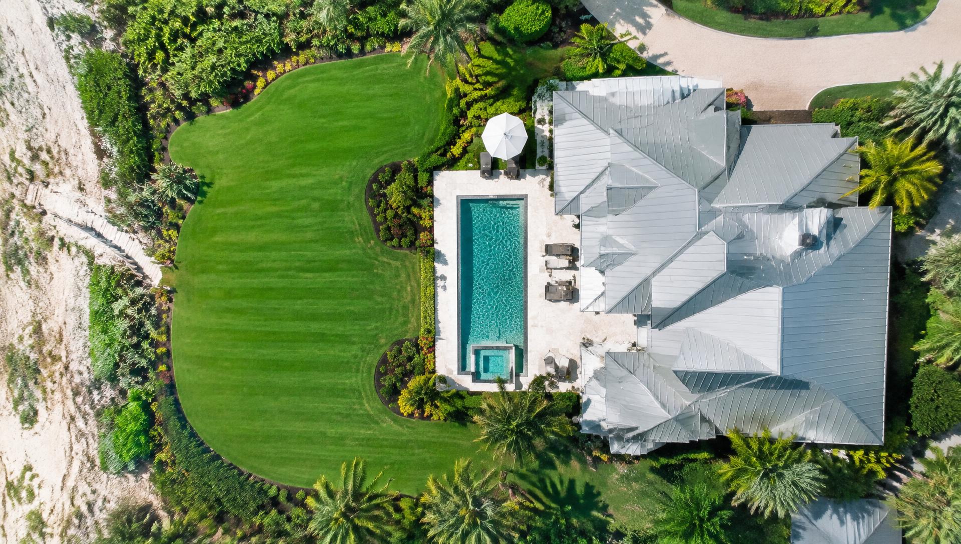 Overhead view of a striped lawn and manicured beds around a coastal Florida home with a pool
